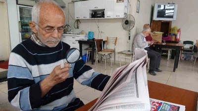 Gazeteleri büyüteçle okuyor
